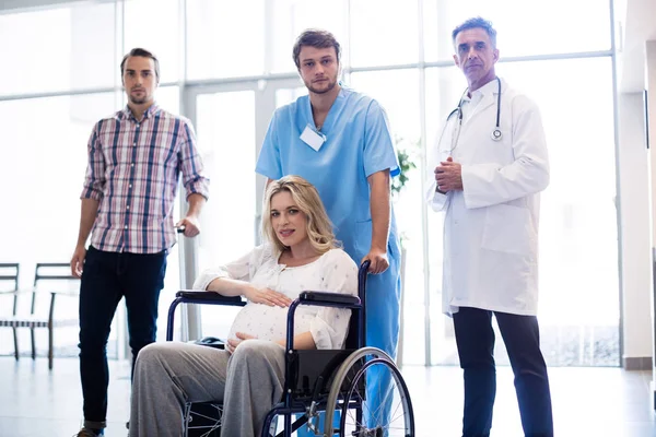 Portrait of smiling doctor carrying pregnant woman in a wheelchair — Stock Photo, Image