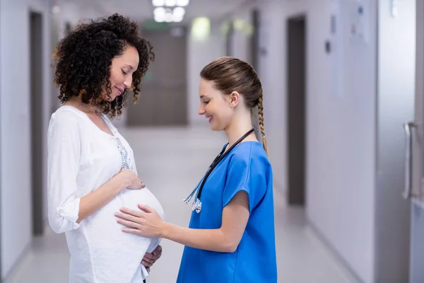 Doctor touching pregnant womans belly in corridor — Stock Photo, Image