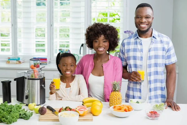 Sonrientes padres e hija tomando un vaso de jugo de naranja en la cocina —  Fotos de Stock