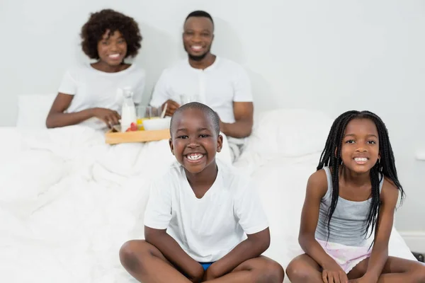 Porträt von Kindern, die lächeln, während Eltern im Hintergrund frühstücken — Stockfoto