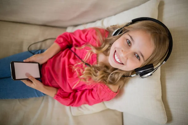 Hymyilevä söpö tyttö kuuntelee musiikkia kuulokkeet olohuoneessa kotona — kuvapankkivalokuva