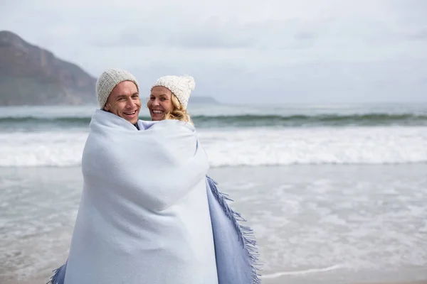 Äldre par insvept i filt på stranden — Stockfoto