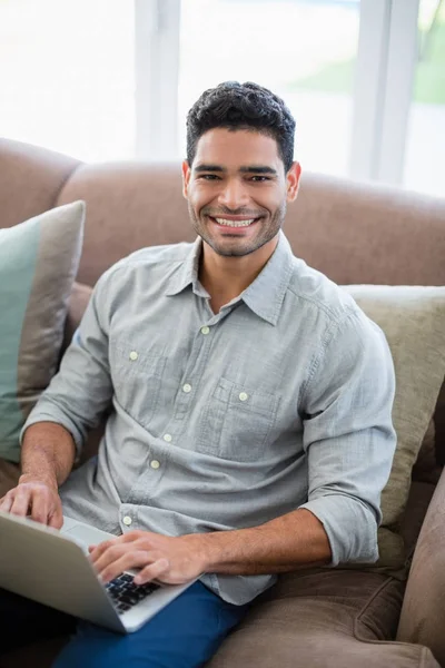 Uomo seduto sul divano e utilizzando il computer portatile in soggiorno a casa — Foto Stock