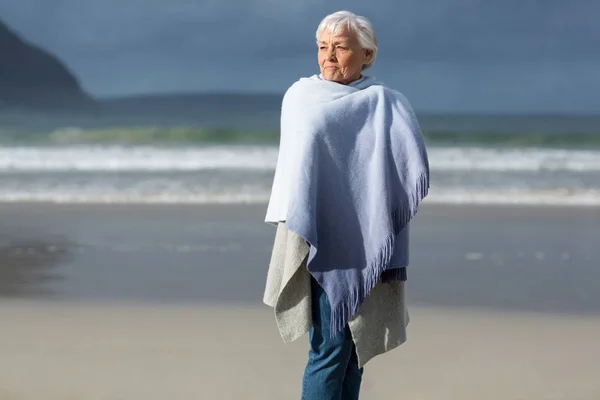 Donna anziana avvolta nello scialle in spiaggia — Foto Stock