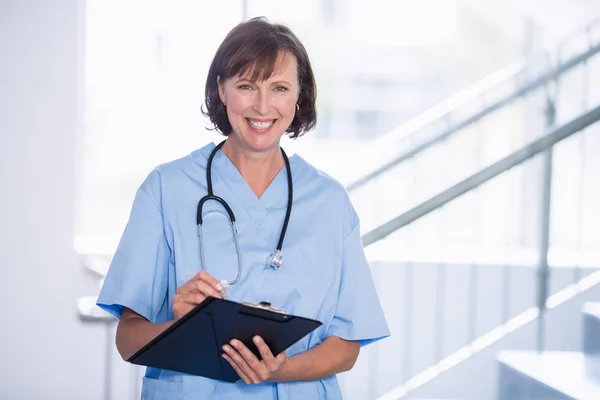 Retrato del médico sonriente escribiendo en el portapapeles en el pasillo —  Fotos de Stock