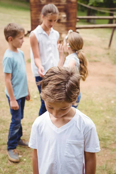 Menino perturbado com amigos fofocando no fundo — Fotografia de Stock