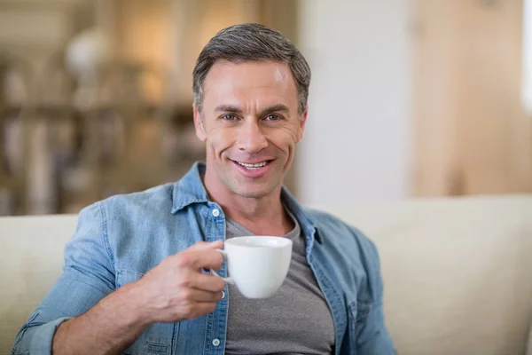 Portret van glimlachende man met koffie in de woonkamer — Stockfoto
