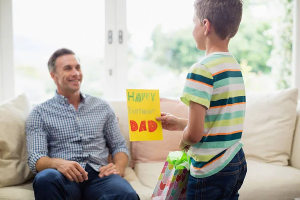 Hijo dando tarjeta de cumpleaños al padre en la sala de estar — Foto de Stock