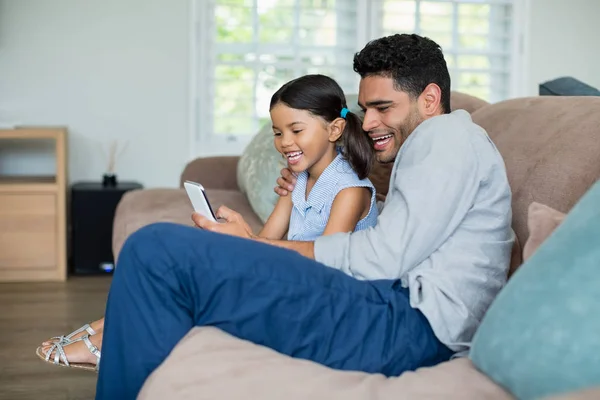 Far och dotter sitter på soffan och med mobiltelefon — Stockfoto