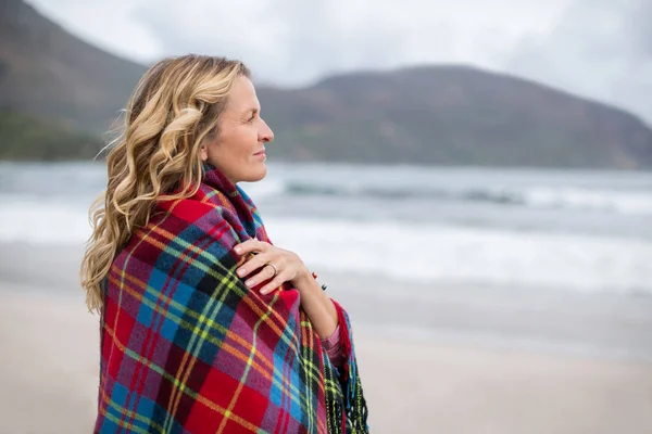 Rijpe vrouw gewikkeld in sjaal op het strand — Stockfoto