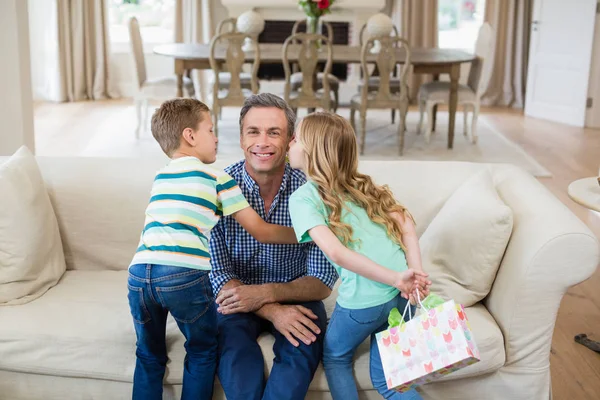 Hijo e hija besando a su padre en la mejilla en la sala de estar — Foto de Stock