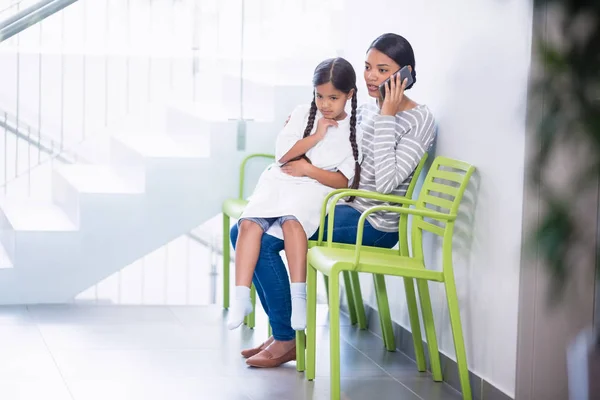 Moeder praten op mobiele telefoon terwijl meisje op haar schoot zit — Stockfoto