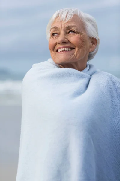 Femme âgée enveloppée dans un châle à la plage — Photo