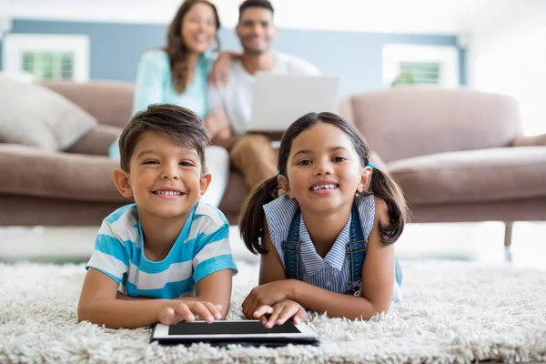 Broers en zussen met behulp van digitale tablet liggend op de rug in de huiskamer — Stockfoto