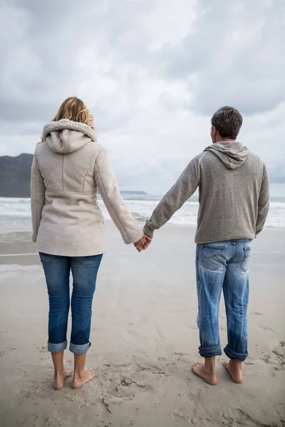Coppia in piedi con mani in mano sulla spiaggia — Foto Stock
