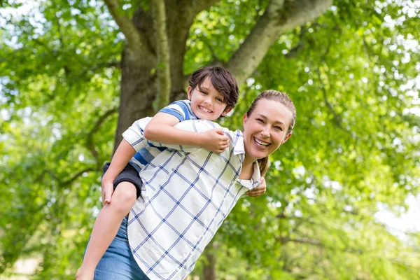 Mor ger en piggyback rida till hennes son i park — Stockfoto