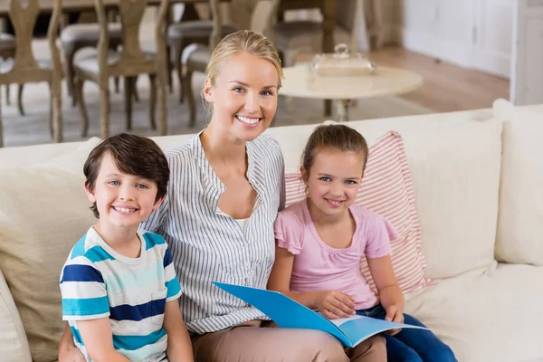 Mãe e crianças sentadas no sofá com livro na sala de estar — Fotografia de Stock