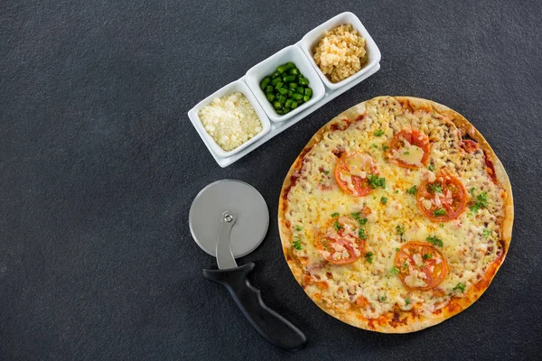 Pizza with pizza cutter and ingredients