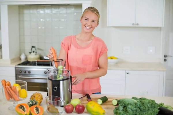 Smiling woman preparing fresh fruit juice in kitchen — Stock Photo, Image