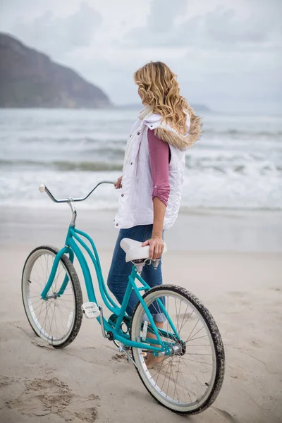 Mujer madura de pie con bicicleta en la playa — Foto de Stock