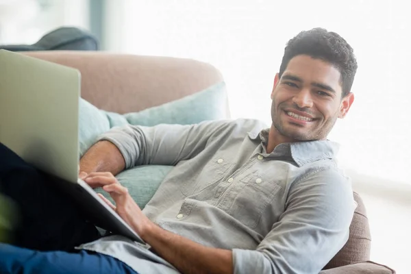 Мужчина сидит на диване и использует ноутбук в гостиной на дому — стоковое фото