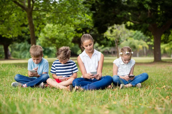 Niños usando teléfono móvil en el parque — Foto de Stock