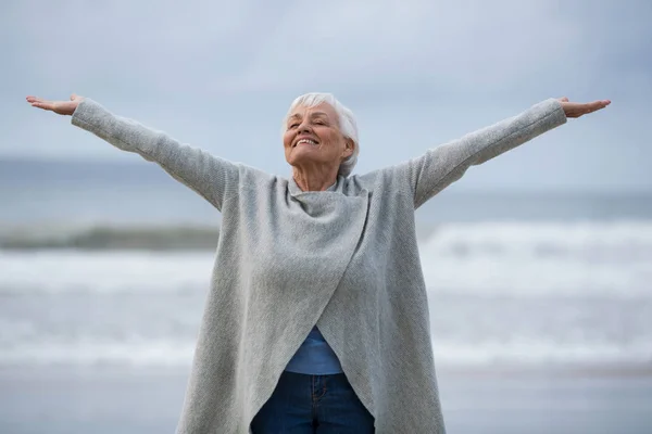 Senior Kvinna med armarna utsträckta stående på stranden — Stockfoto