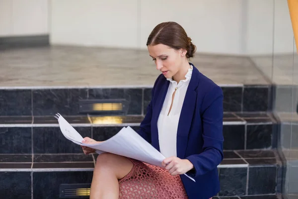 Businesswoman sitting on steps holding blueprint — Stock Photo, Image