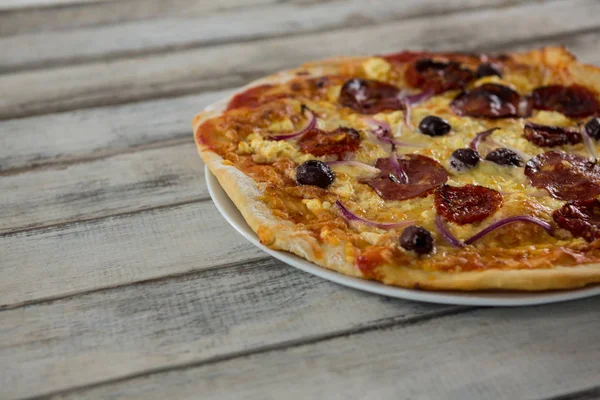 Pizza italiana en un plato sobre una tabla de madera — Foto de Stock