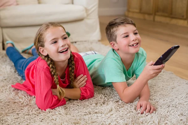 Братья и сестры лежат на ковре и смотрят телевизор в гостиной — стоковое фото