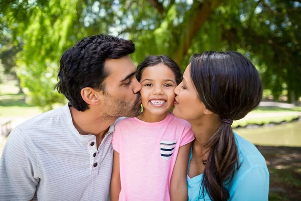 Menina sendo beijada por seus pais no parque — Fotografia de Stock
