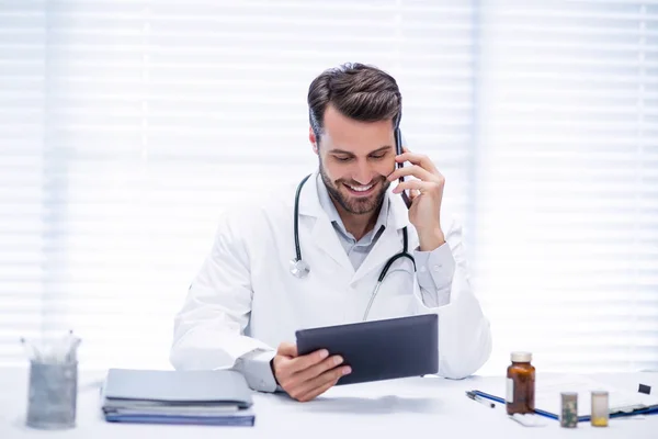 Médecin masculin parlant sur un téléphone mobile tout en utilisant une tablette numérique — Photo