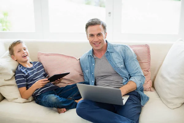 Father and son using laptop and digital tablet in living room — Stock Photo, Image