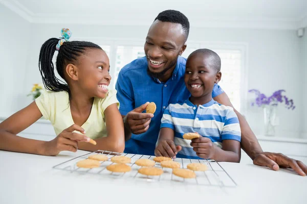 Sorrindo pai e filhos comendo biscoitos em casa — Fotografia de Stock