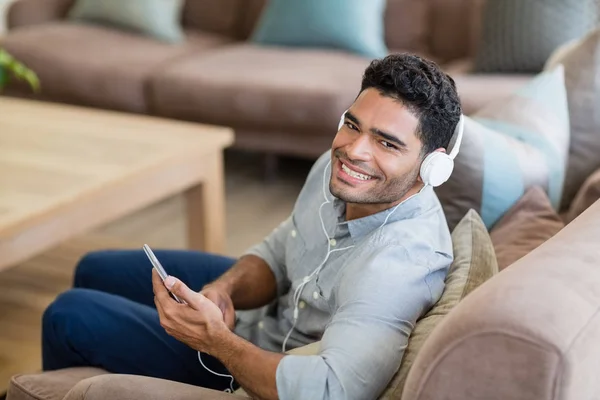 Hombre escuchando música en el teléfono móvil en la sala de estar en casa —  Fotos de Stock