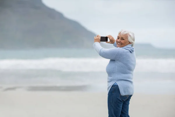 Seniorin fotografiert Landschaft mit Handy am Strand — Stockfoto