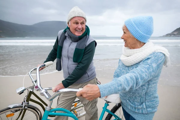 Senior paar staande met fietsen op het strand — Stockfoto