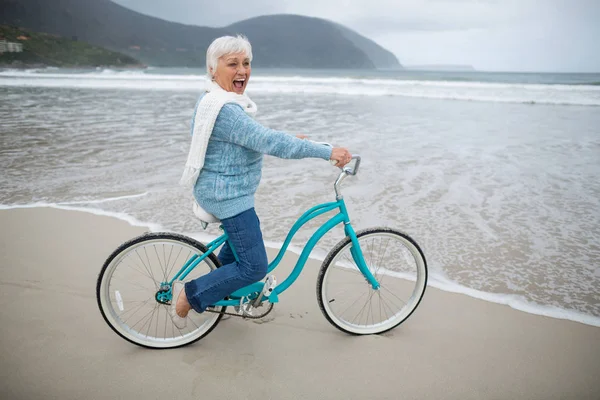 Senior woman riding bicycle on the beach — Stock Photo, Image