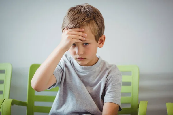 Portrait of upset boy sitting on chair in corridor — Stock Photo, Image