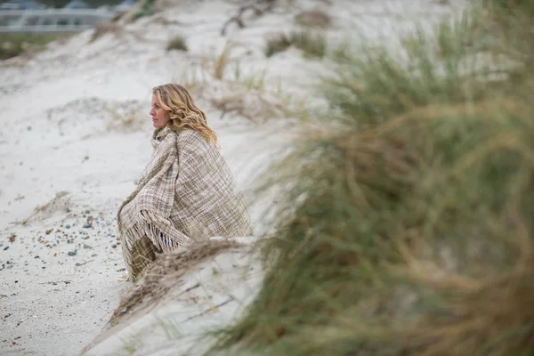 Зрелая женщина, завернутая в шаль на пляже — стоковое фото