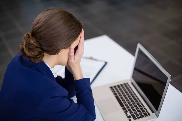 Zmęczona kobieta siedzi przy biurku z laptopa — Zdjęcie stockowe