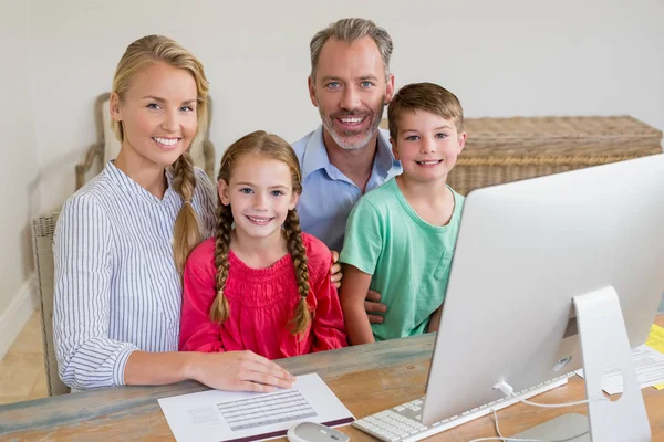 Familia feliz sentado en el escritorio con el ordenador — Foto de Stock