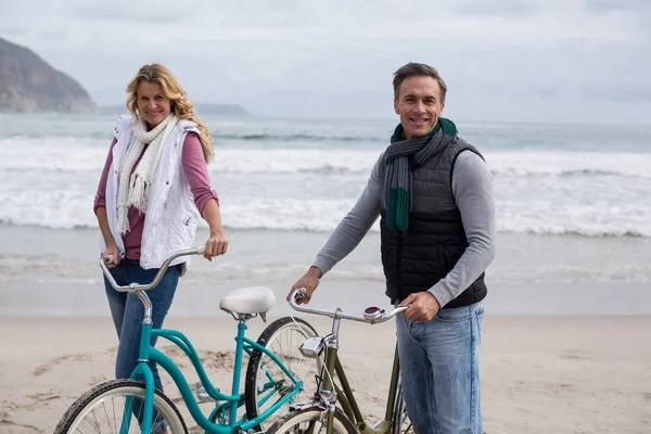 Coppia matura in piedi con le biciclette sulla spiaggia — Foto Stock