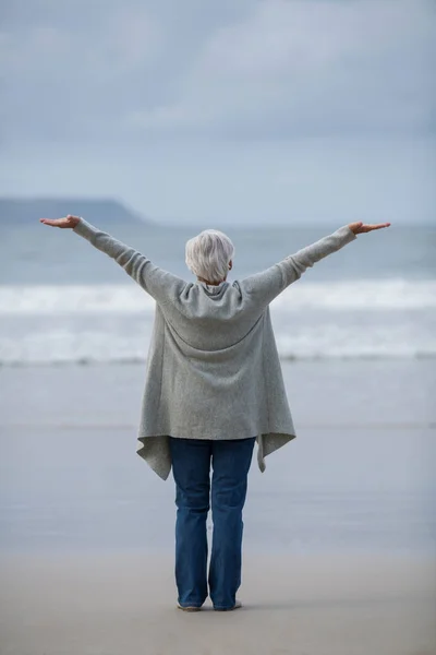 Senior Kvinna med armarna utsträckta stående på stranden — Stockfoto