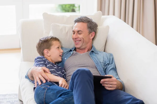 Père et fils couchés sur canapé avec tablette numérique dans le salon — Photo