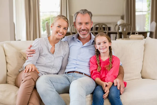Retrato de padres sonrientes e hija sentados en el sofá en la sala de estar —  Fotos de Stock