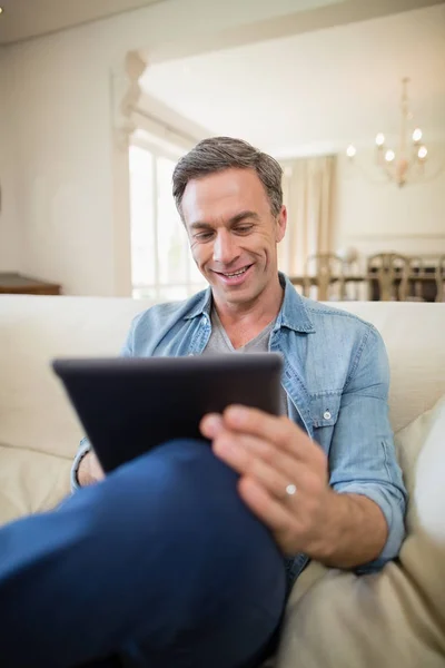 Мужчина, сидящий на диване и использующий цифровой планшет в гостиной — стоковое фото