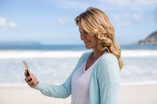 Mujer madura tomando una selfie desde el teléfono móvil en la playa —  Fotos de Stock