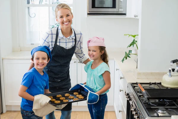 Madre e bambini che tengono vassoio di biscotti al forno in cucina — Foto Stock