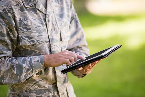 Midtsnitt av en soldat som bruker digitale nettbrett i parken – stockfoto